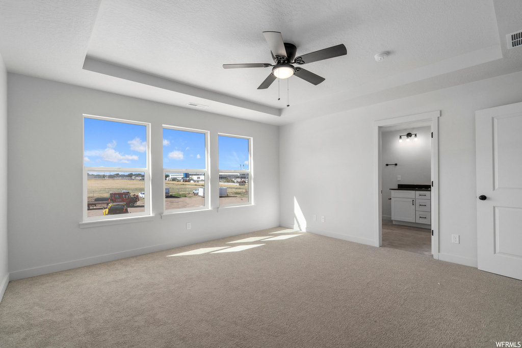 Carpeted spare room featuring a tray ceiling and ceiling fan