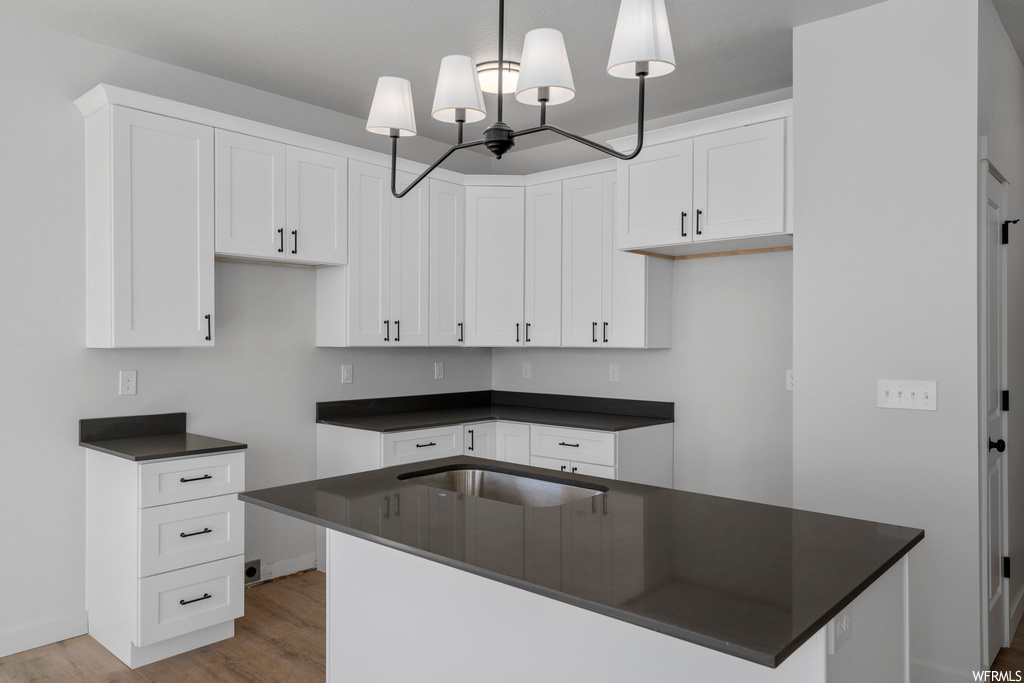 Kitchen with white cabinets, light wood-type flooring, pendant lighting, and a chandelier