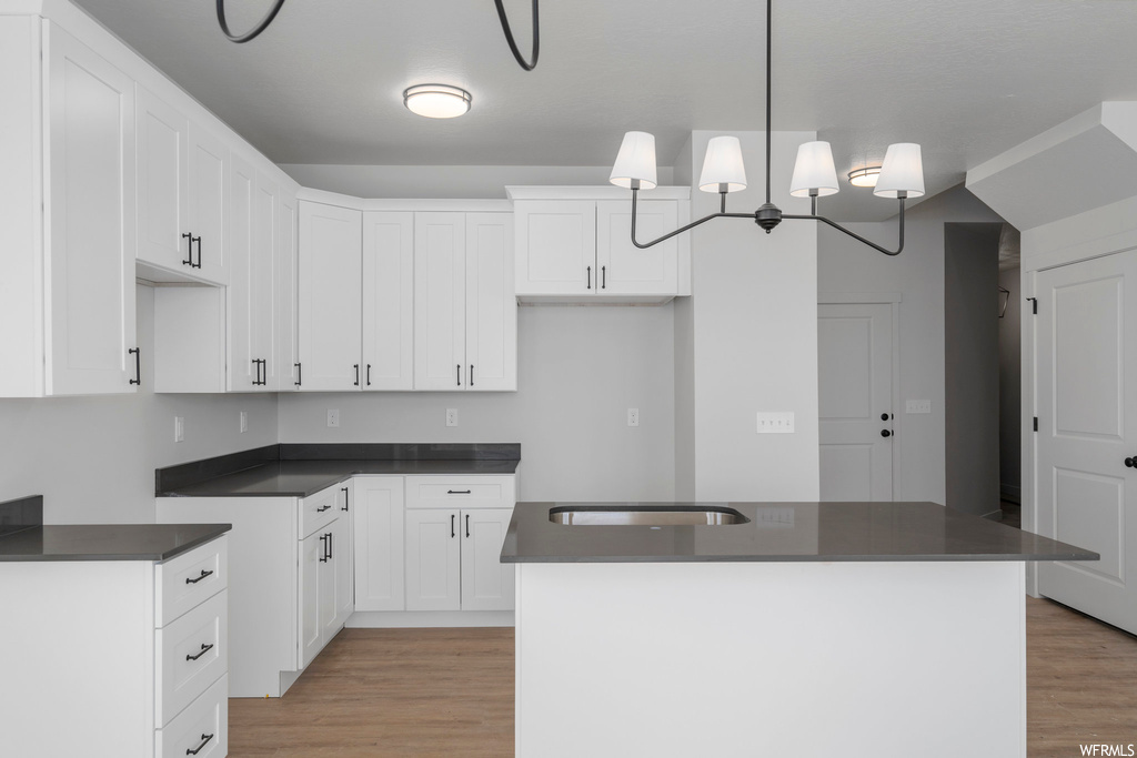 Kitchen featuring a center island, light hardwood / wood-style floors, a chandelier, and white cabinetry