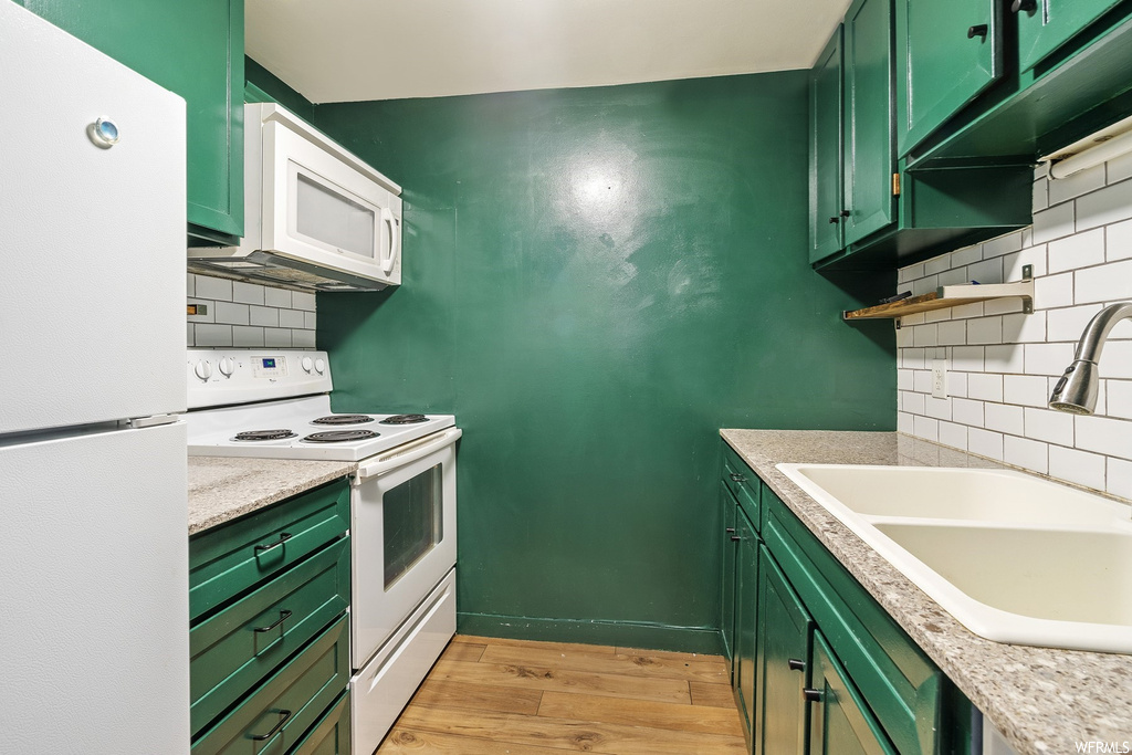 Kitchen featuring green cabinets, white appliances, sink, and light hardwood / wood-style floors