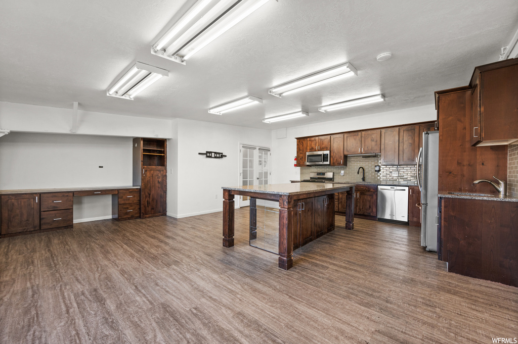 Kitchen featuring dark wood-type flooring, tasteful backsplash, a kitchen island, and appliances with stainless steel finishes