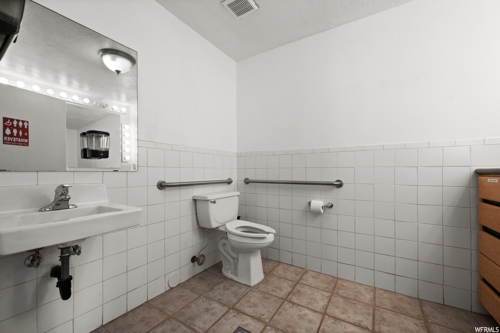 Bathroom with toilet, tile floors, tile walls, and sink