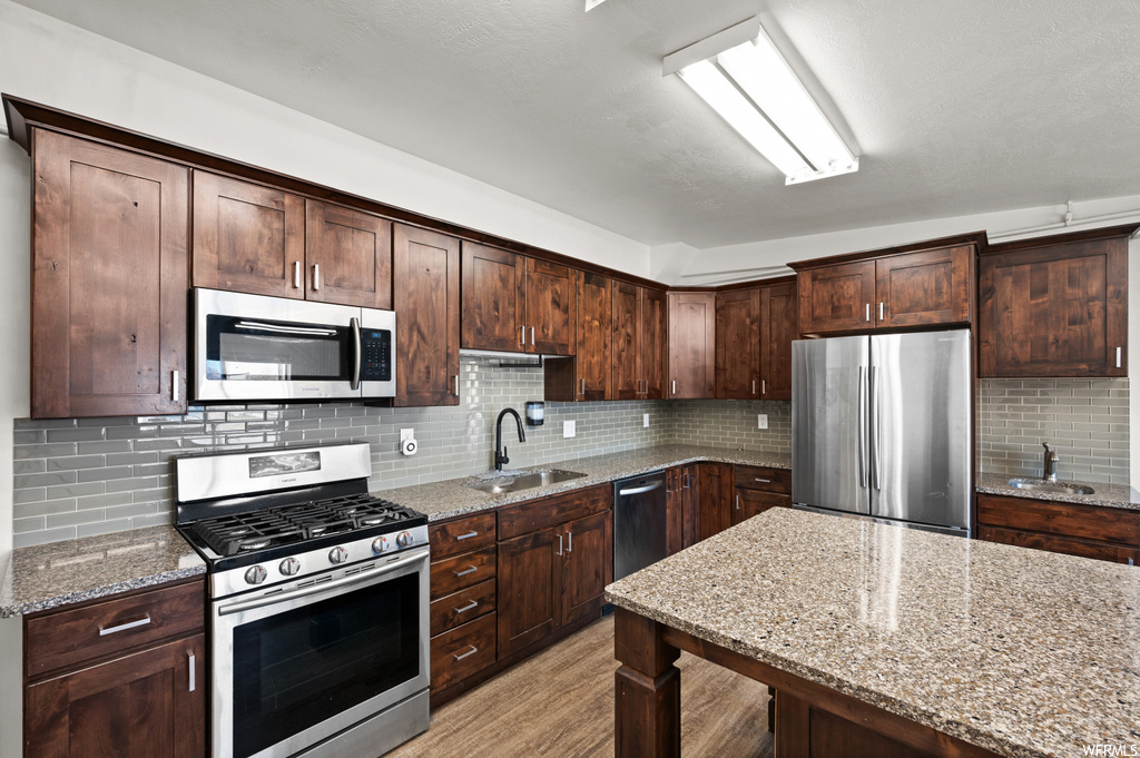 Kitchen featuring sink, light stone countertops, stainless steel appliances, and backsplash