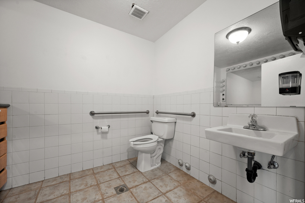 Bathroom with toilet, tile flooring, sink, and tile walls