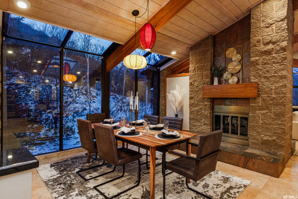 Tiled dining room featuring wooden ceiling, lofted ceiling with beams, and a stone fireplace