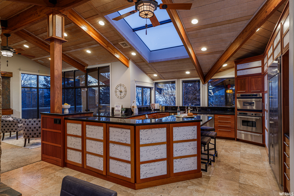 Kitchen featuring light tile floors, ceiling fan, and vaulted ceiling with skylight