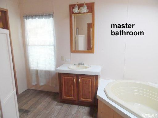 Bathroom with tiled bath, large vanity, and hardwood / wood-style flooring