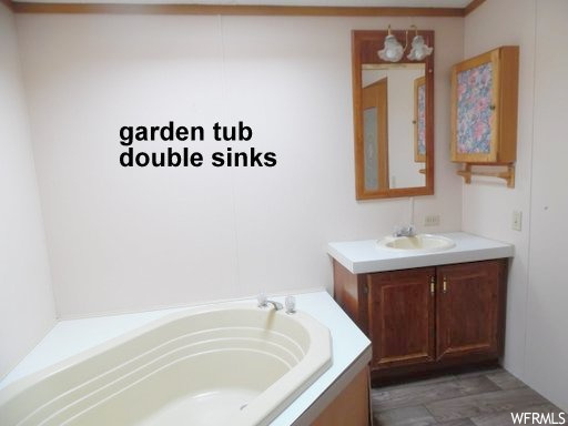 Bathroom with vanity with extensive cabinet space, a bath to relax in, and hardwood / wood-style flooring