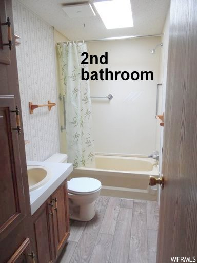 Full bathroom with shower / bath combination with curtain, vanity, toilet, and wood-type flooring