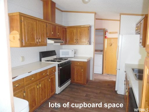 Kitchen featuring dark hardwood / wood-style flooring, washer / dryer, sink, and white appliances
