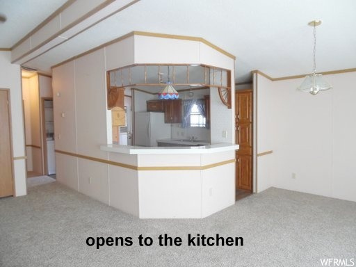 Kitchen with a chandelier, pendant lighting, kitchen peninsula, light colored carpet, and white fridge