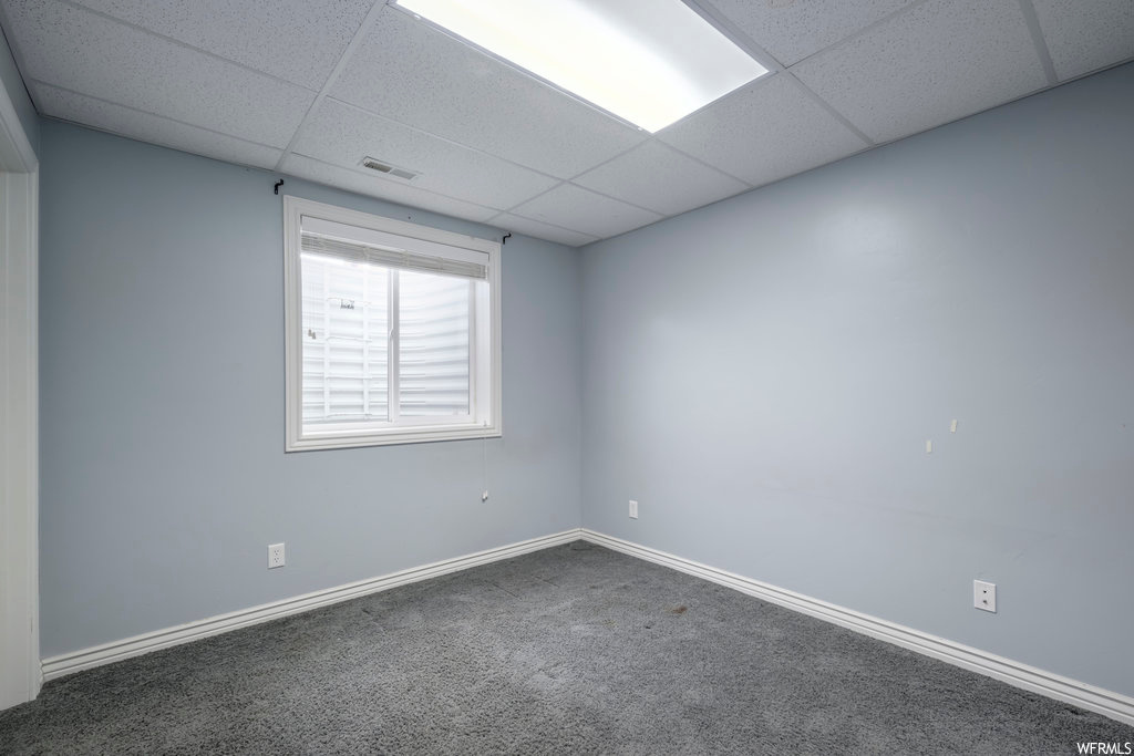 Spare room featuring dark colored carpet and a drop ceiling