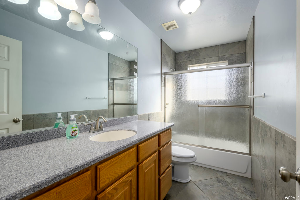 Full bathroom featuring toilet, oversized vanity, tile flooring, shower / bath combination with glass door, and an inviting chandelier