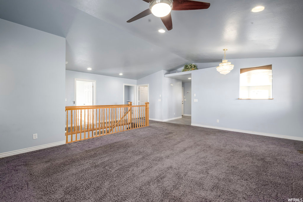 Empty room with lofted ceiling, ceiling fan with notable chandelier, and carpet floors