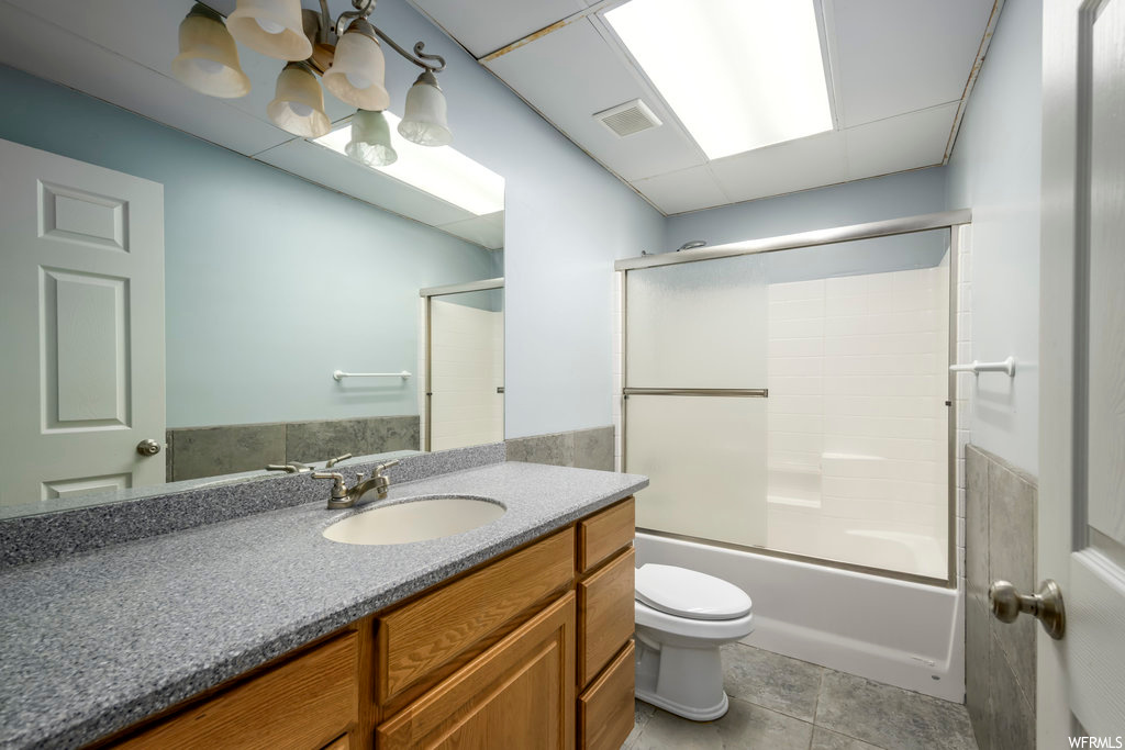 Full bathroom with tile flooring, toilet, enclosed tub / shower combo, and large vanity