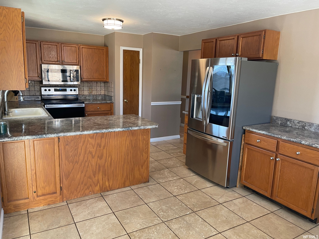 Kitchen featuring light tile floors, sink, stainless steel appliances, and backsplash