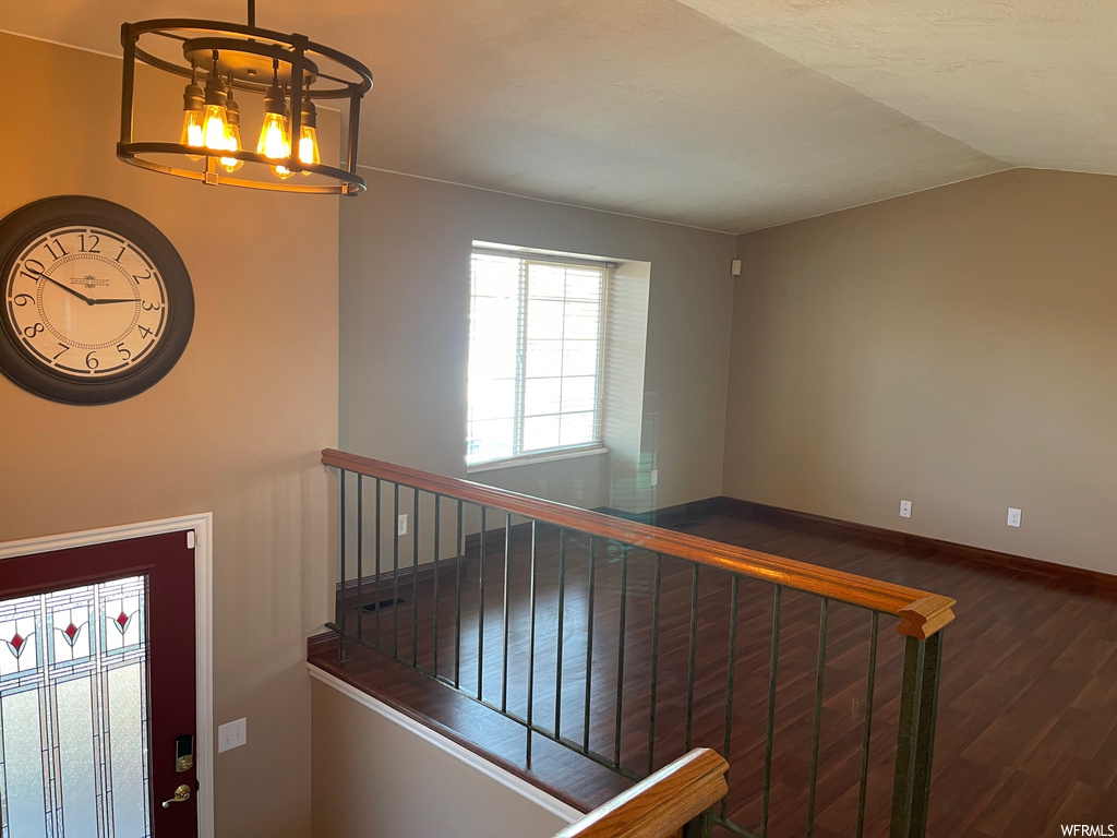 Staircase featuring a notable chandelier, dark wood-type flooring, and vaulted ceiling