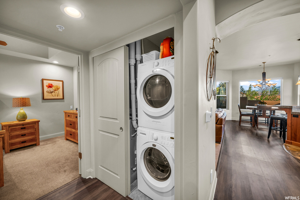 Laundry room with dark carpet, a chandelier, and stacked washer / drying machine