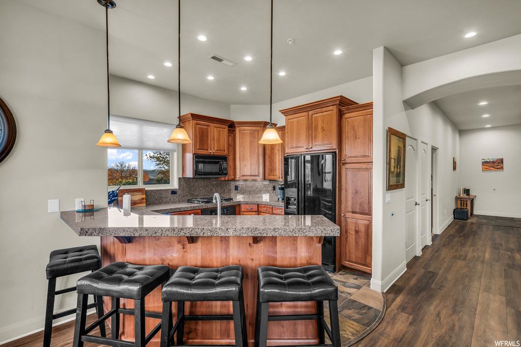 Kitchen featuring hanging light fixtures, dark wood-type flooring, a breakfast bar, black appliances, and tasteful backsplash