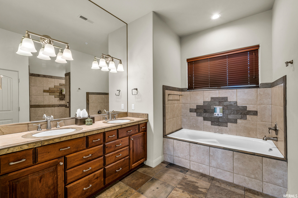 Bathroom featuring tiled bath, double sink vanity, and tile flooring