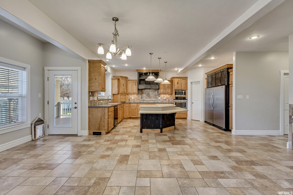 Kitchen featuring appliances with stainless steel finishes, decorative light fixtures, backsplash, light tile floors, and a kitchen island