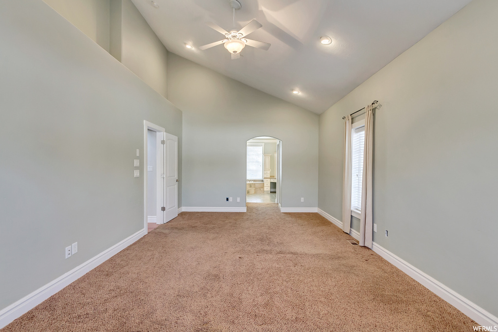 Empty room featuring light colored carpet, ceiling fan, and high vaulted ceiling