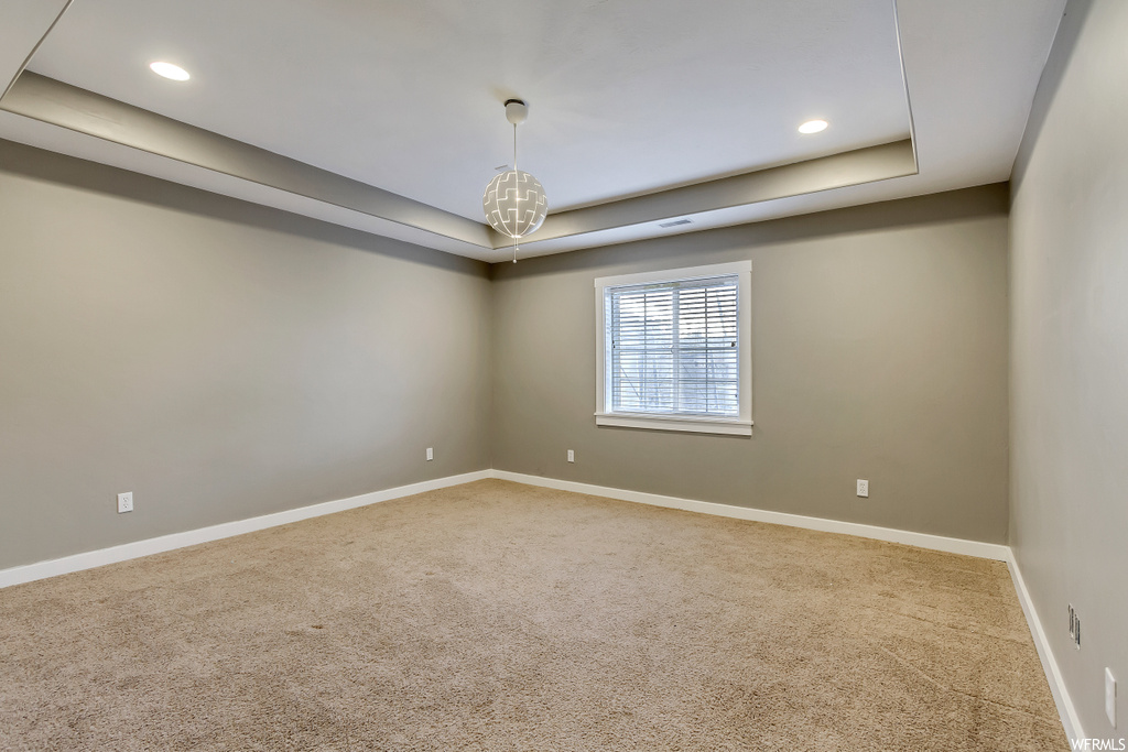 Unfurnished room featuring a tray ceiling, carpet, and an inviting chandelier
