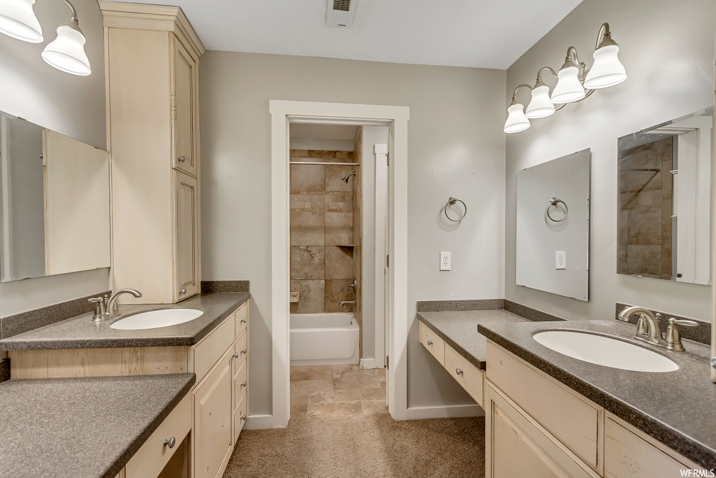Bathroom with tiled shower / bath combo, tile floors, and double sink vanity