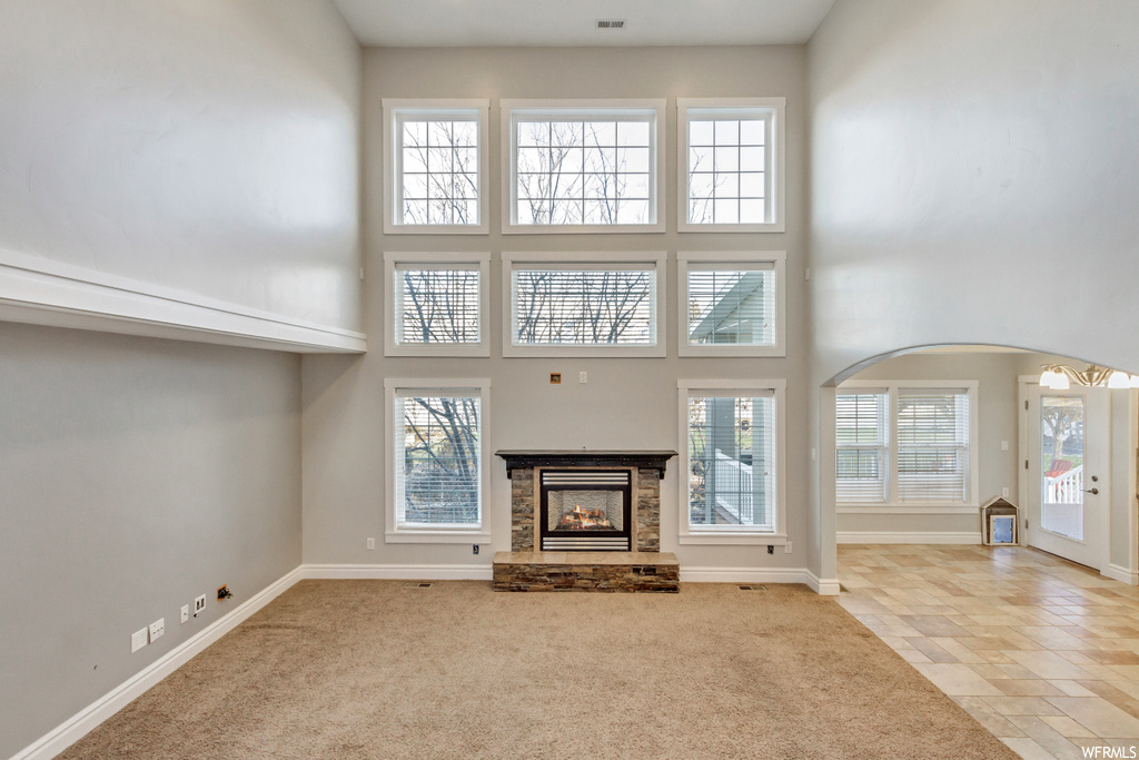 Unfurnished living room with light carpet, plenty of natural light, a stone fireplace, and a towering ceiling