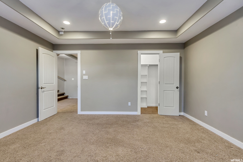 Unfurnished bedroom with a closet, light colored carpet, a walk in closet, and a notable chandelier
