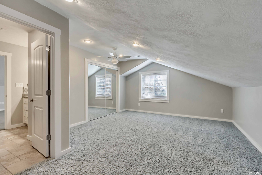 Additional living space with light tile floors, ceiling fan, a textured ceiling, and vaulted ceiling
