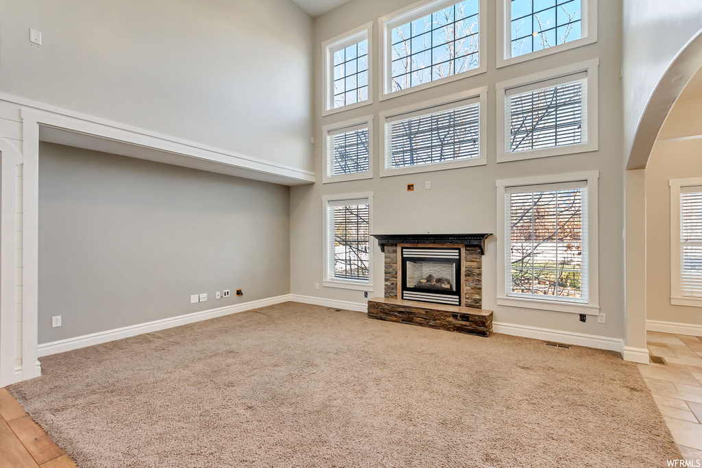 Unfurnished living room featuring a high ceiling, light colored carpet, and a stone fireplace