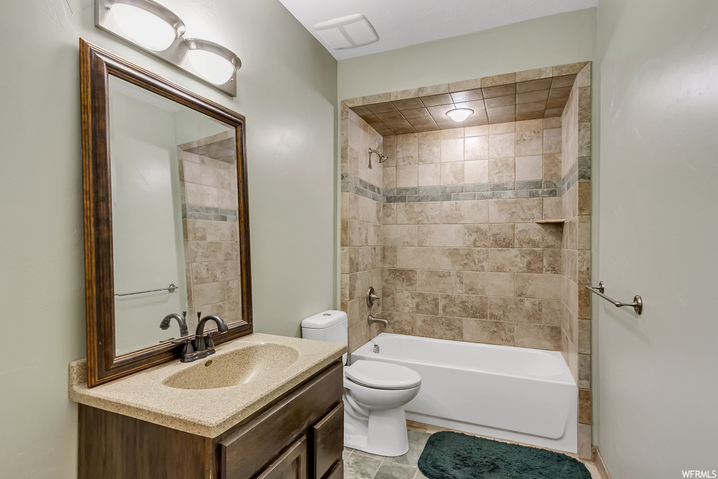 Full bathroom with toilet, tile flooring, tiled shower / bath, and vanity with extensive cabinet space
