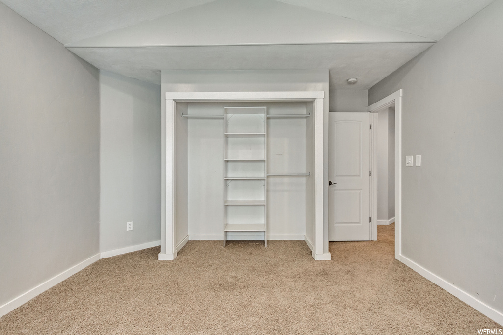 Unfurnished bedroom featuring lofted ceiling, light colored carpet, and a closet