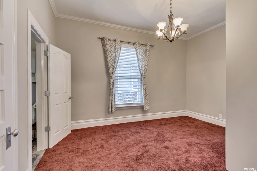 Carpeted spare room with ornamental molding and a notable chandelier