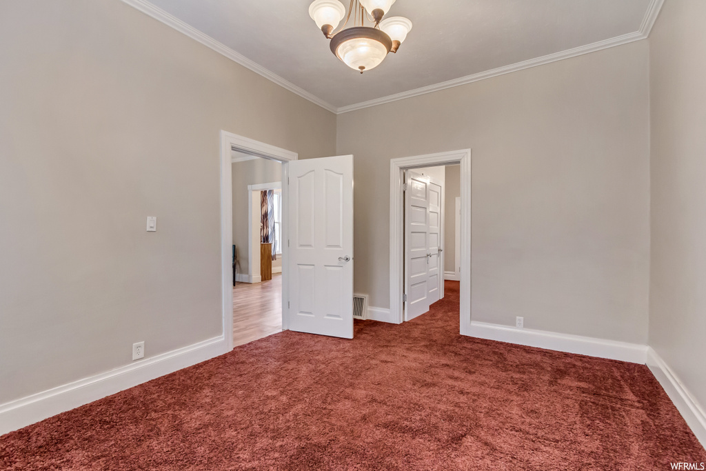 Carpeted spare room with ornamental molding and an inviting chandelier