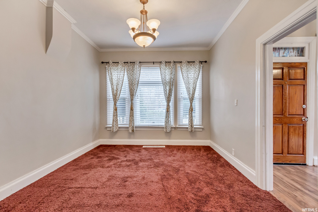 Empty room featuring ornamental molding, a notable chandelier, and light colored carpet