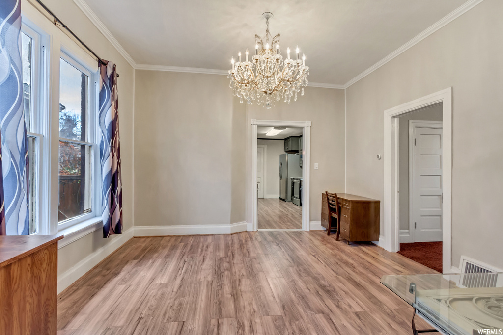 Empty room with a chandelier, light wood-type flooring, and crown molding