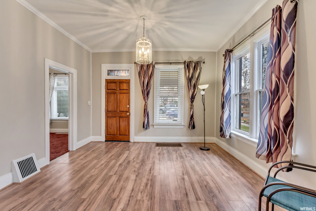 Foyer entrance with ornamental molding, light hardwood / wood-style floors, and a notable chandelier