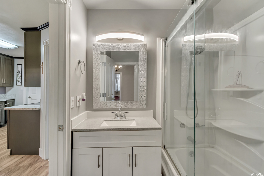 Bathroom featuring combined bath / shower with glass door, oversized vanity, and wood-type flooring