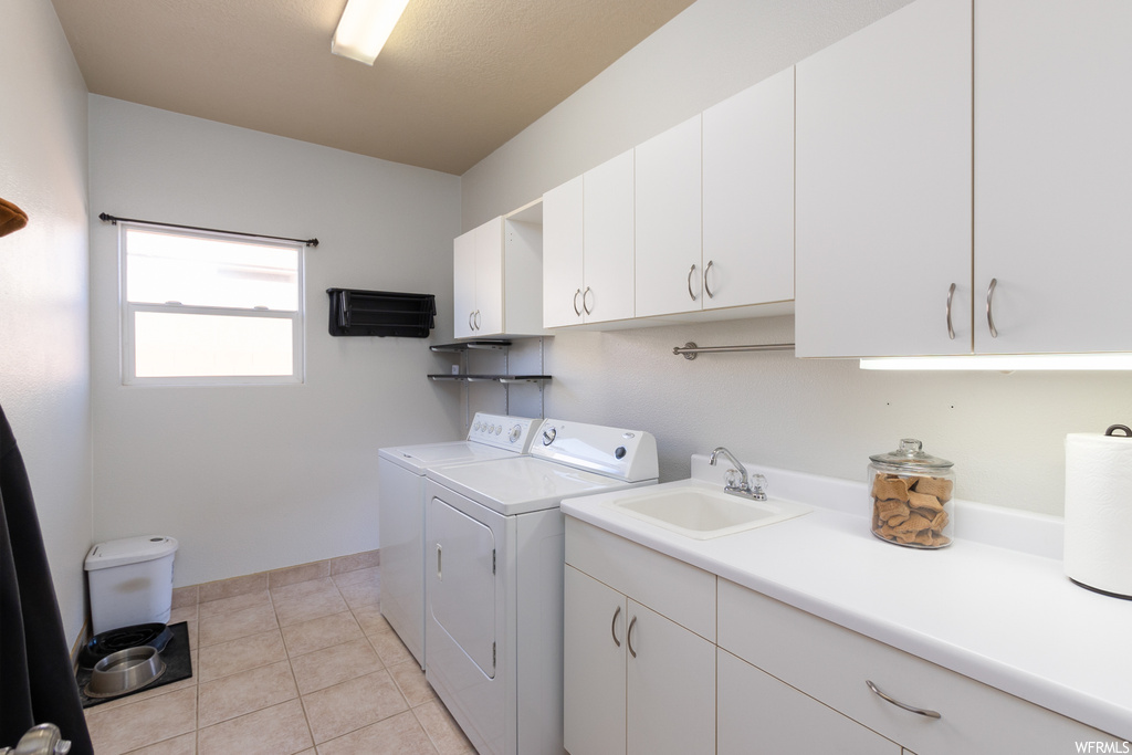 Laundry area featuring cabinets, sink, washing machine and dryer, and light tile flooring