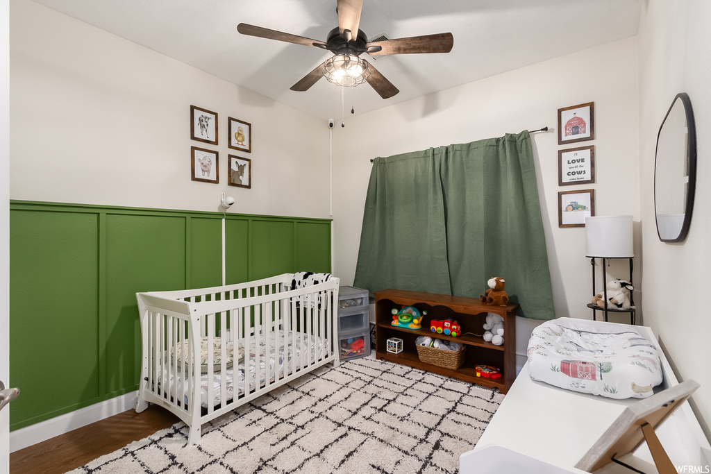 Bedroom featuring ceiling fan, a nursery area, and light hardwood / wood-style floors