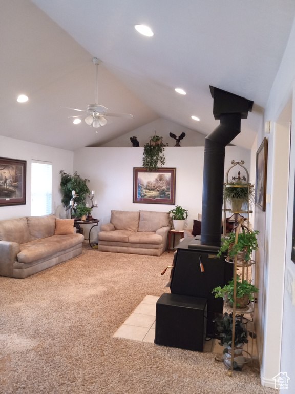 Living room featuring vaulted ceiling, ceiling fan, a wood stove, and light carpet
