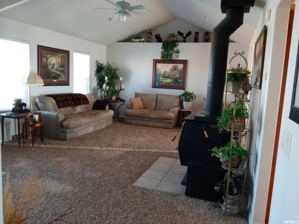 Living room with ceiling fan, lofted ceiling, a wood stove, and light colored carpet