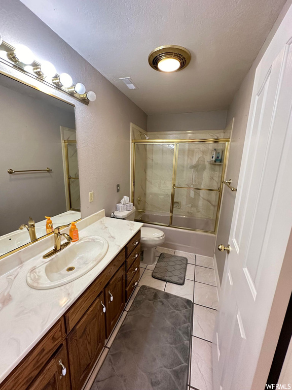 Full bathroom featuring toilet, a textured ceiling, combined bath / shower with glass door, tile floors, and vanity
