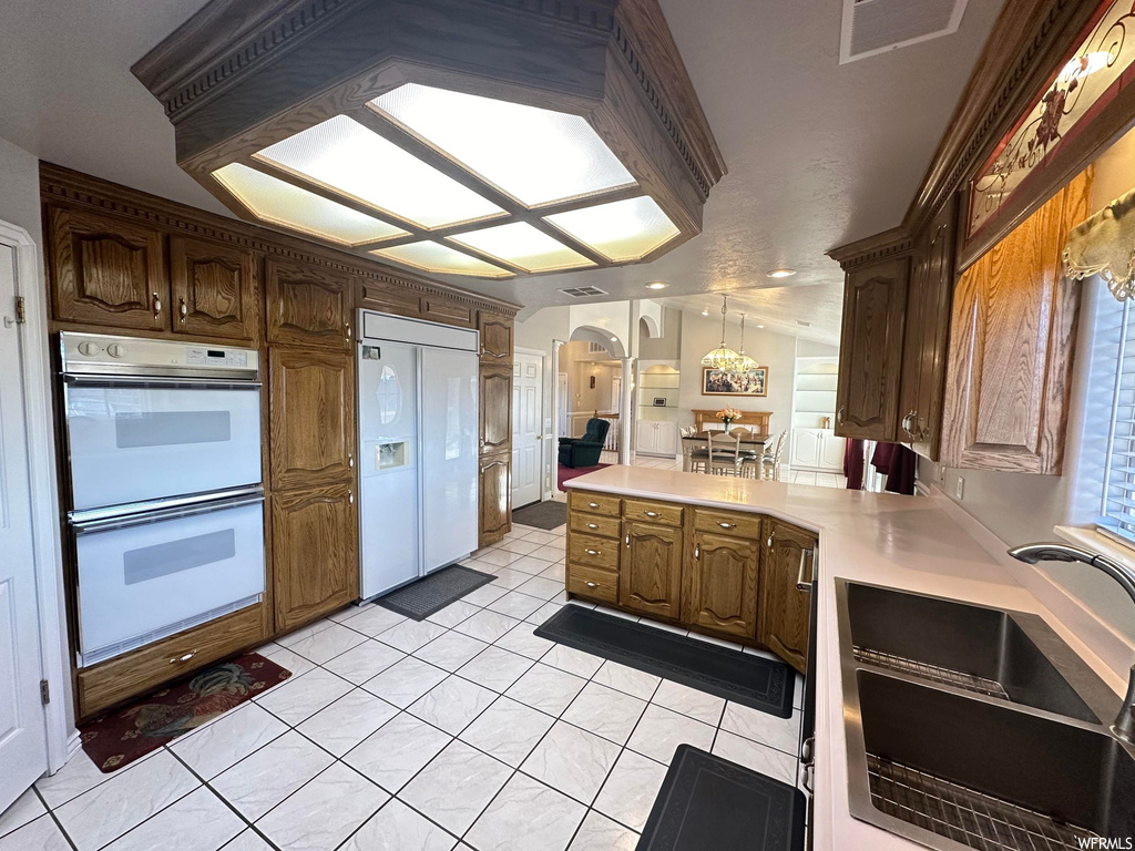 Kitchen featuring light tile floors, paneled refrigerator, sink, hanging light fixtures, and white double oven