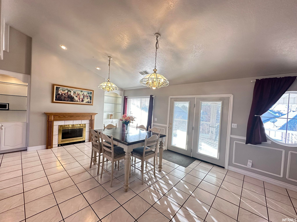 Dining space featuring a notable chandelier, vaulted ceiling, built in shelves, light tile floors, and a tile fireplace