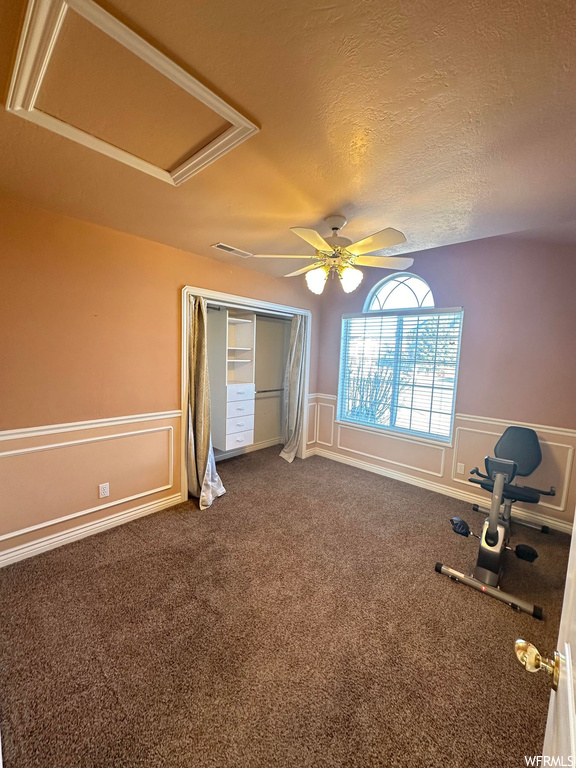 Workout room featuring dark colored carpet, ceiling fan, and a textured ceiling