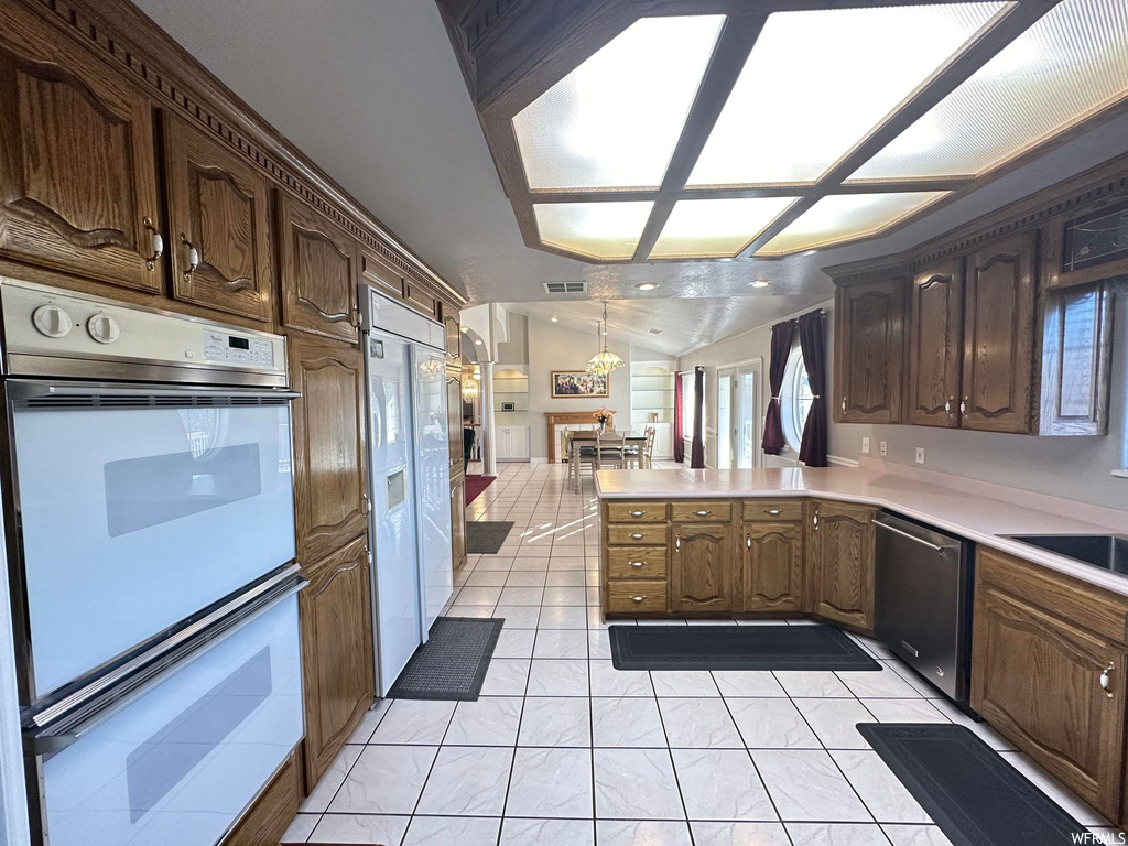 Kitchen featuring white double oven, dishwasher, decorative light fixtures, light tile floors, and kitchen peninsula