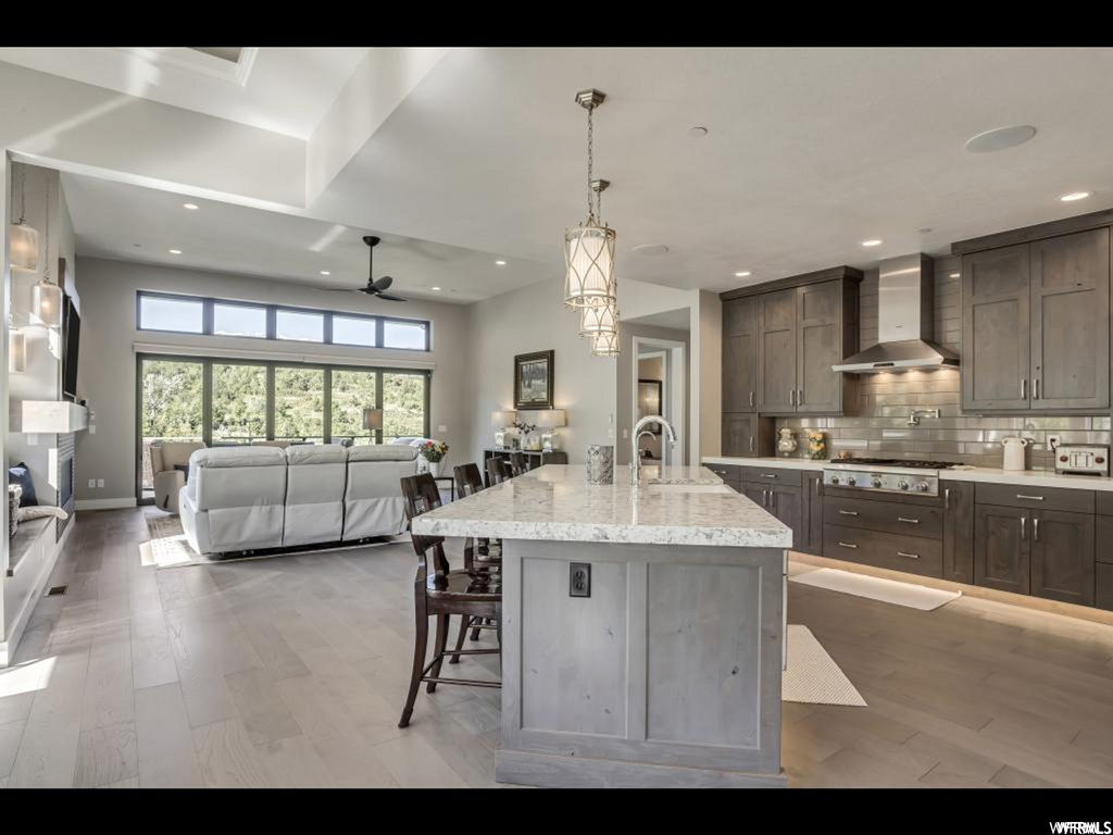 Kitchen with stainless steel gas cooktop, an island with sink, wall chimney range hood, ceiling fan, and a kitchen breakfast bar